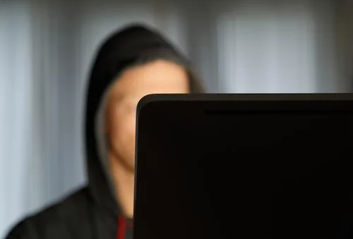 hooded man behind a computer monitor.